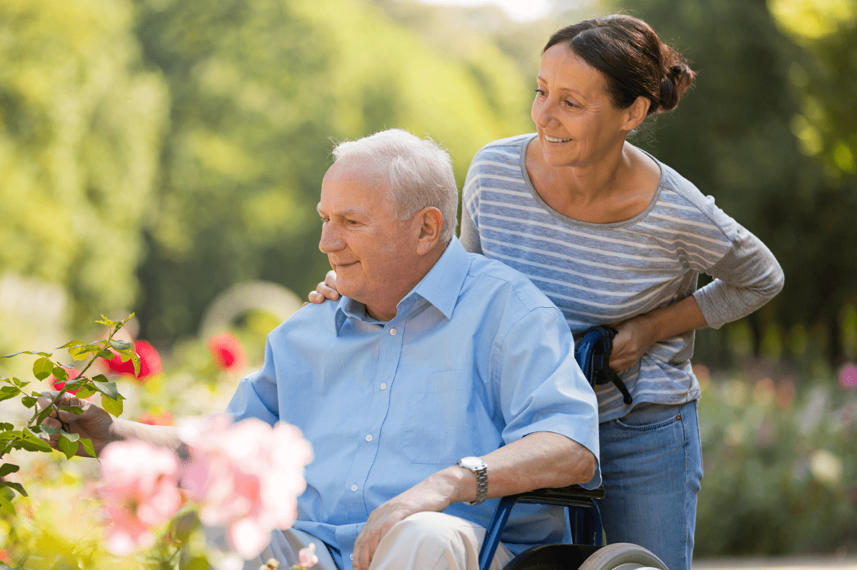 Family Caregiver Volunteer - Woman pushing man in Wheelchair in Garden