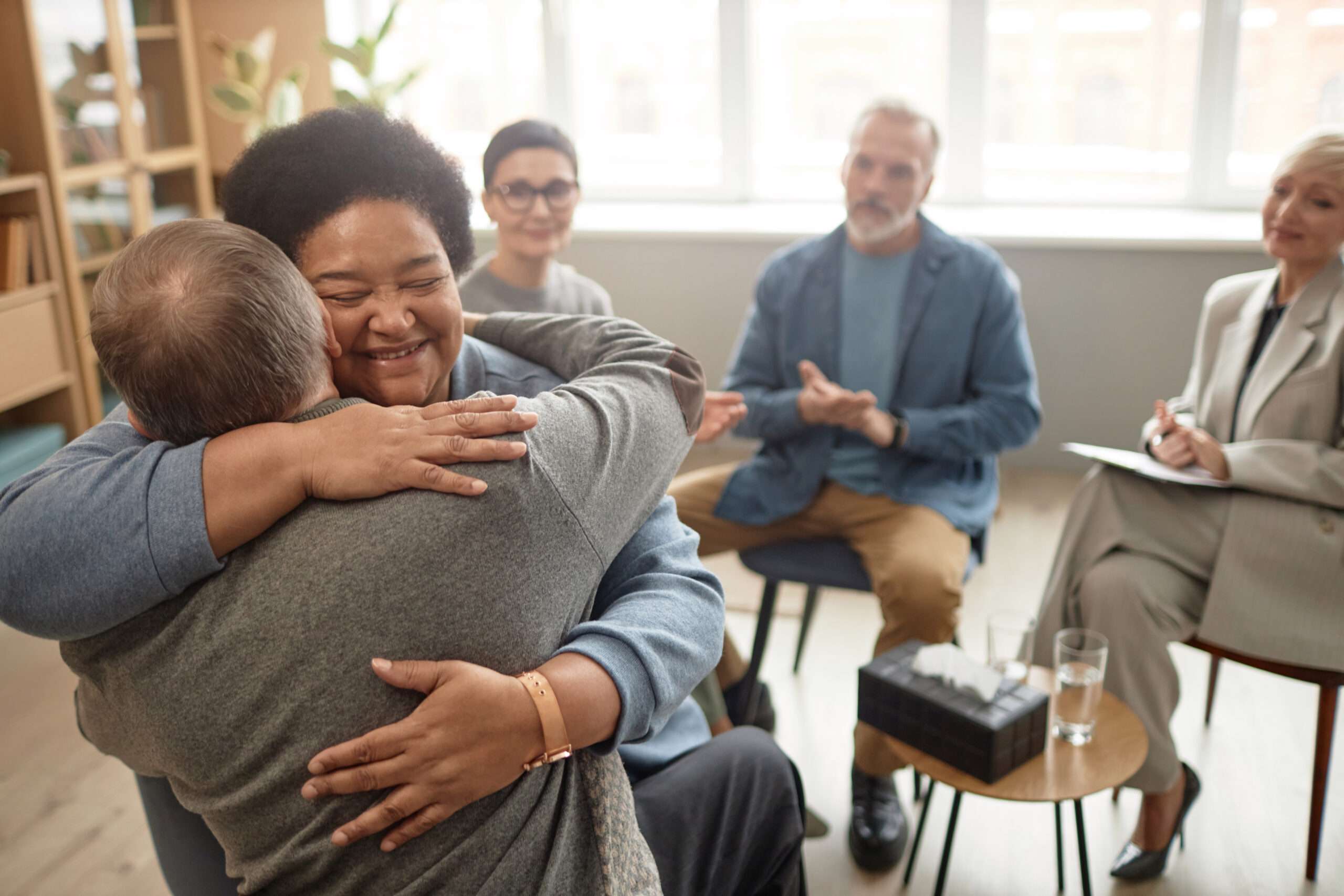 African American Senior Woman Embracing Friend in Group Therapy
