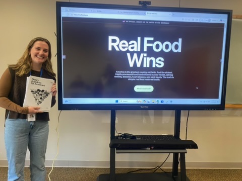 Woman stands in front of screen that reads "Real food wins"